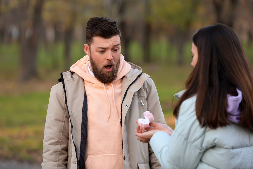 Young woman proposing to her surprised boyfriend in forest