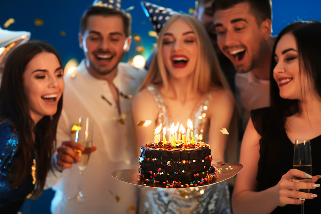 Young woman with tasty cake and her friends at birthday party